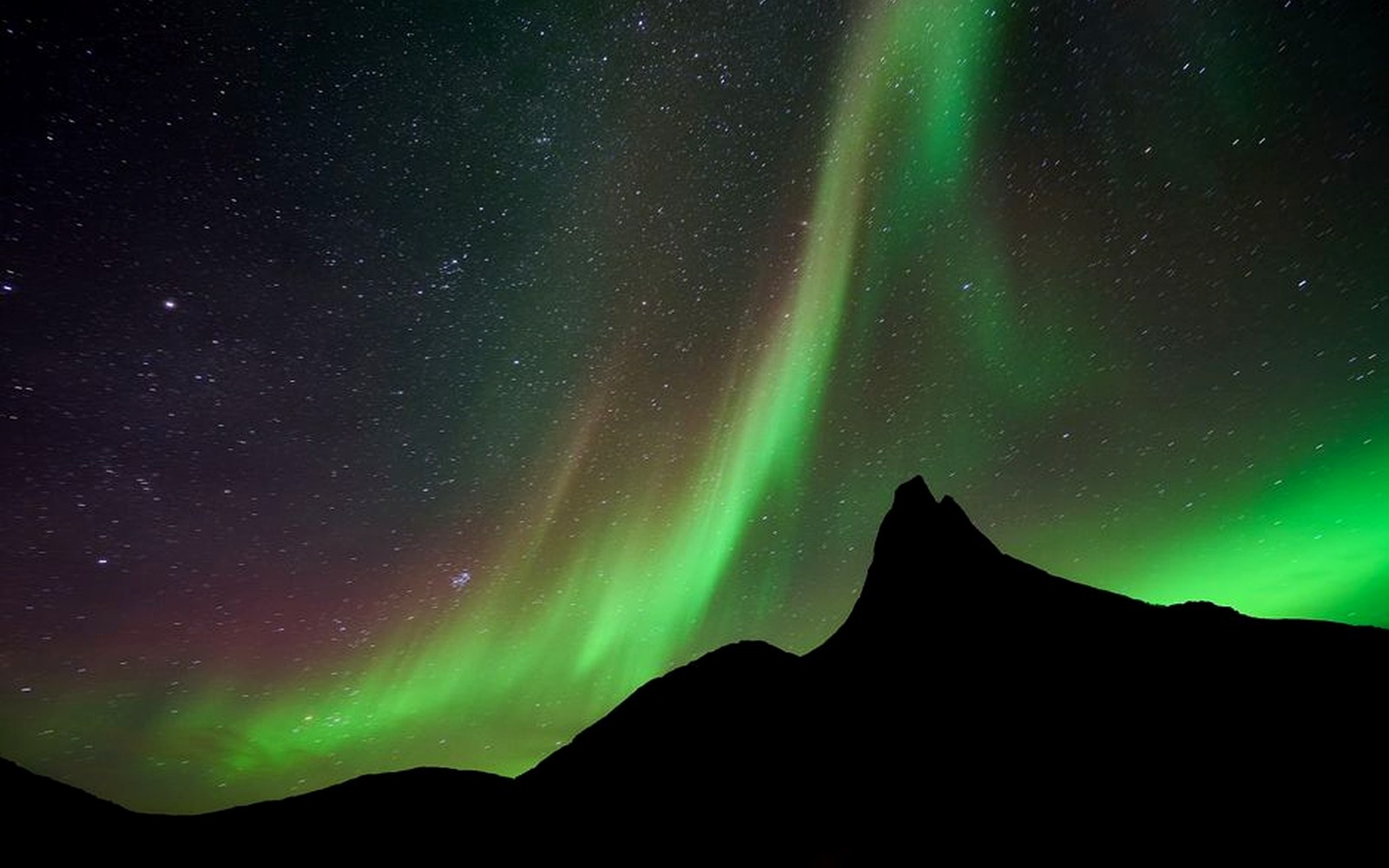 Green aurora glowing above a dark mountain ridge at night.